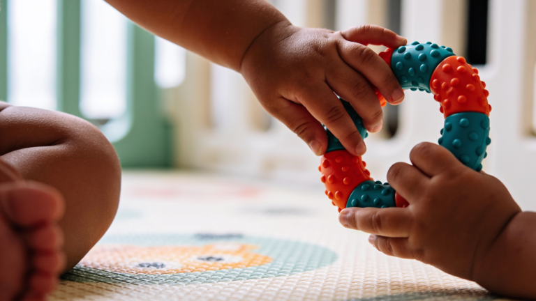 Mãos de bebê explorando textura de brinquedo sensorial colorido