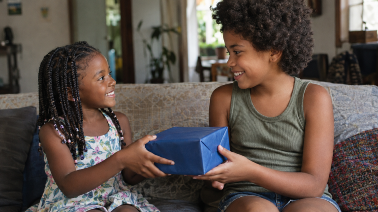 Duas primas sorrindo, uma entregando um embrulho de presente para a outra